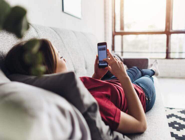 Woman Laying on a Couch Looking at Her Phone